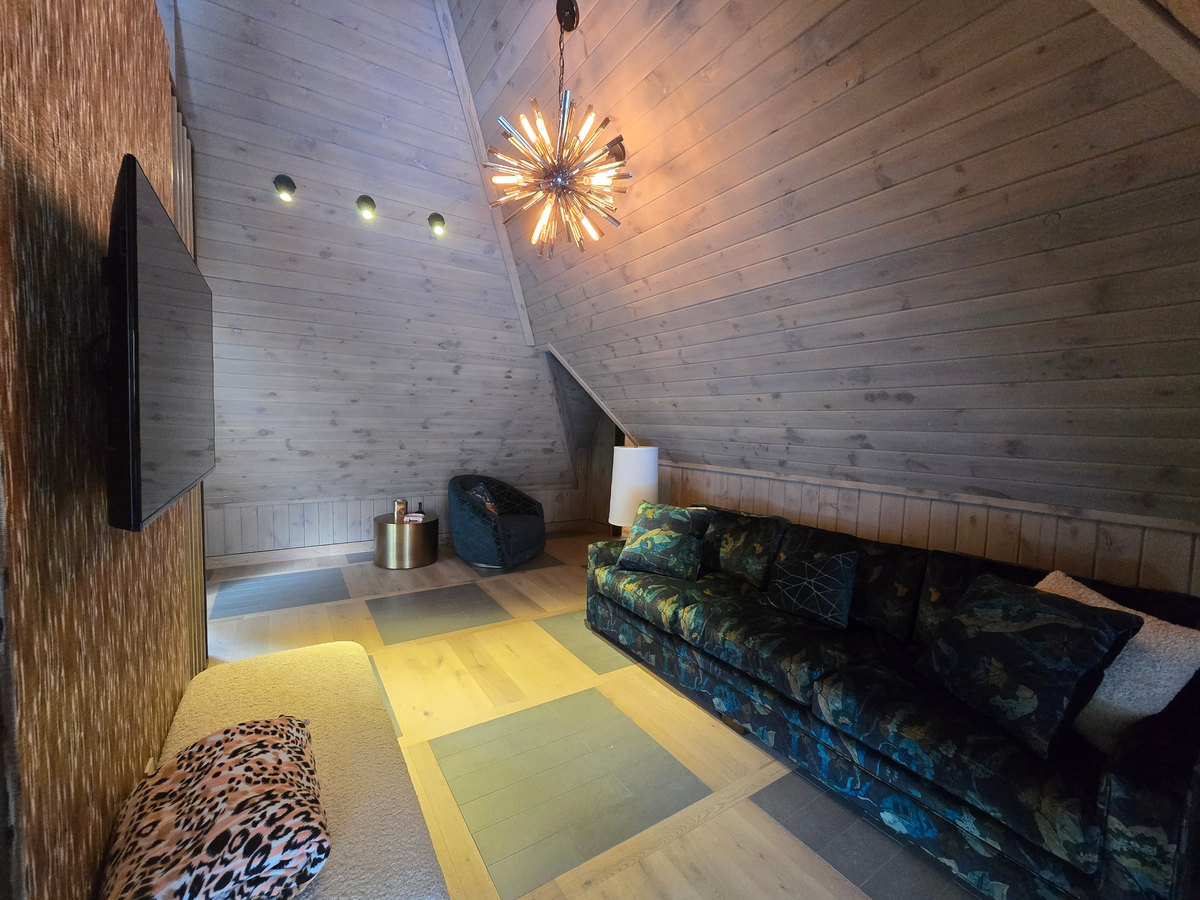 A sitting room with pale wood-clad sloping walls, a chandelier and a dark sofa.