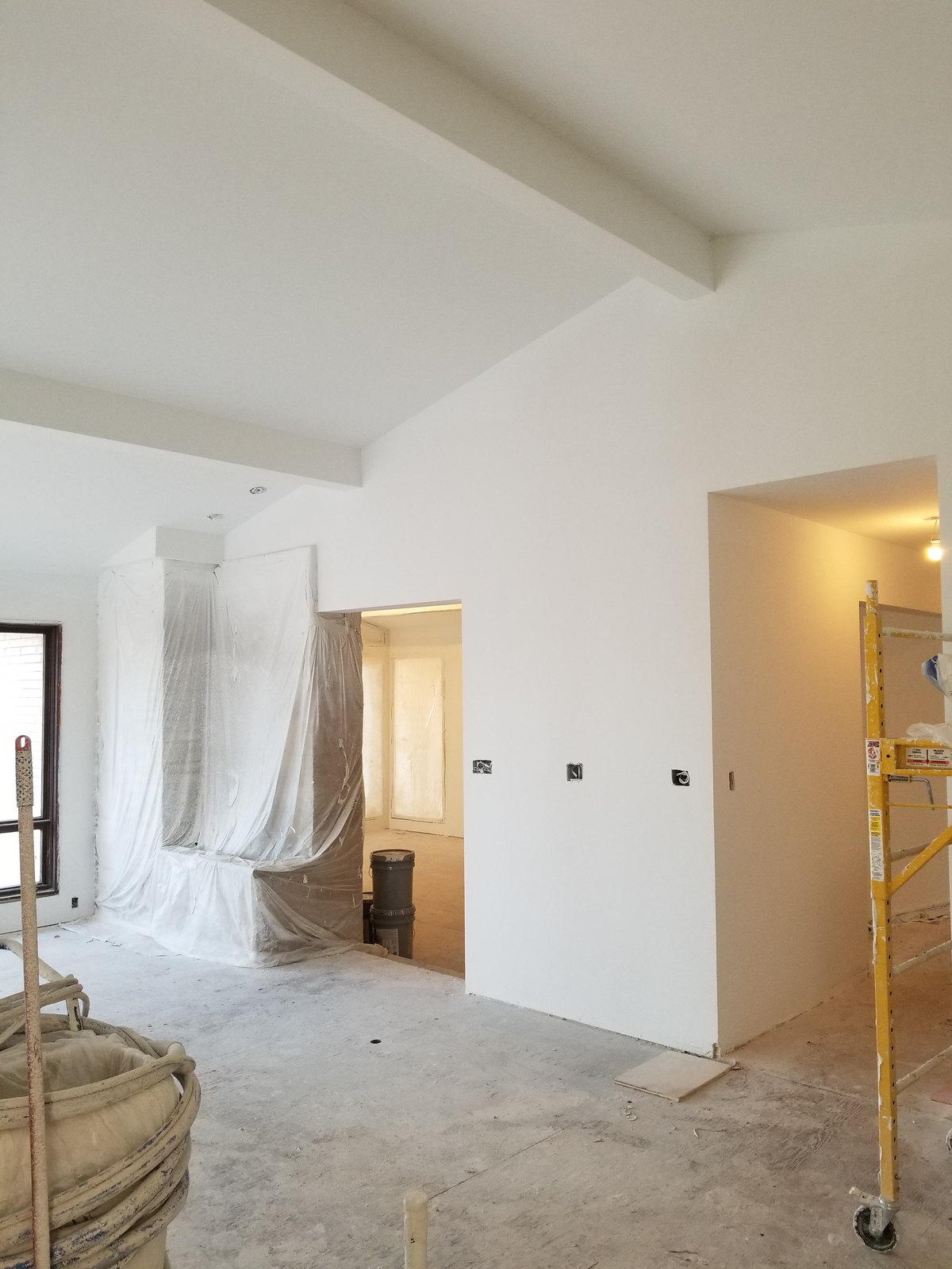 Stepped white ceiling planes above open doorways during interior finishing, with masked surfaces and scaffolding at the edges.