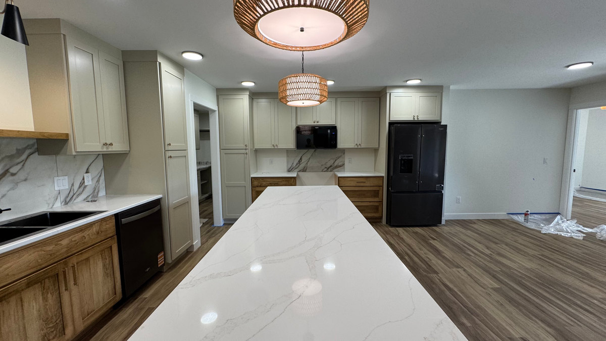 Kitchen with a long white island, light upper cabinets, wood lower cabinets and recessed ceiling lights.