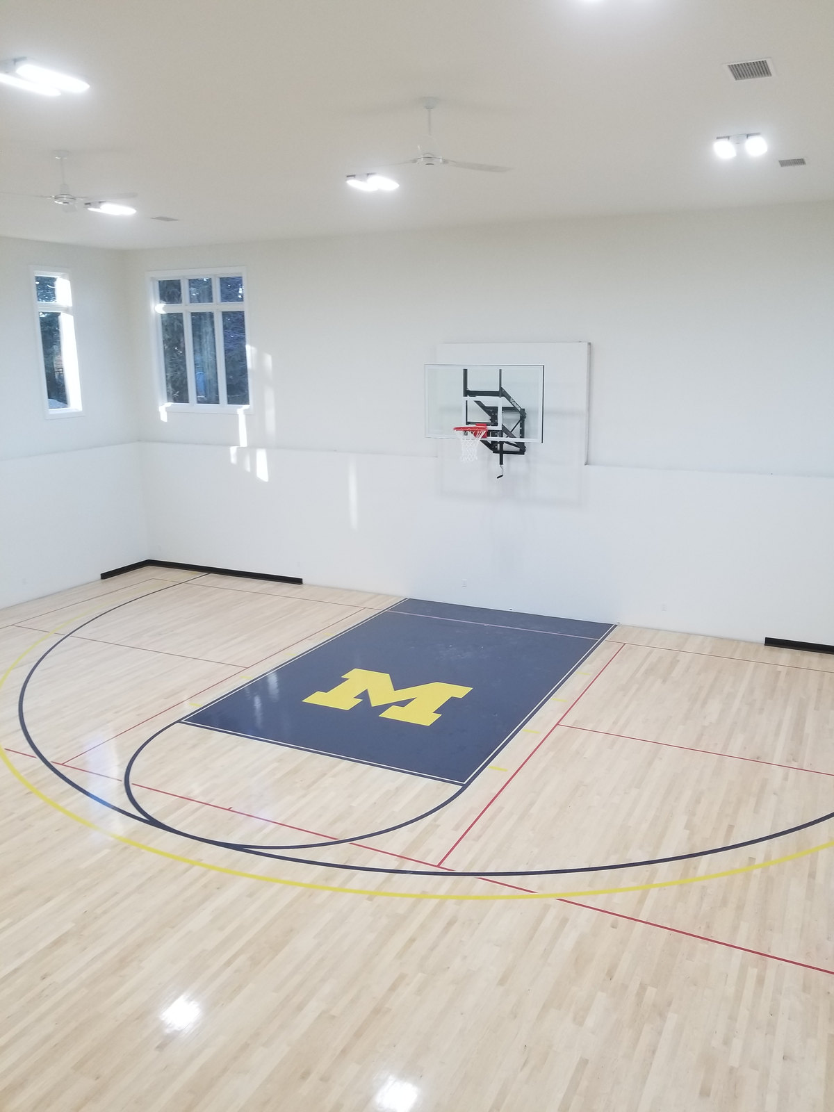 White walls and ceiling above a basketball hoop and a polished wood court floor.