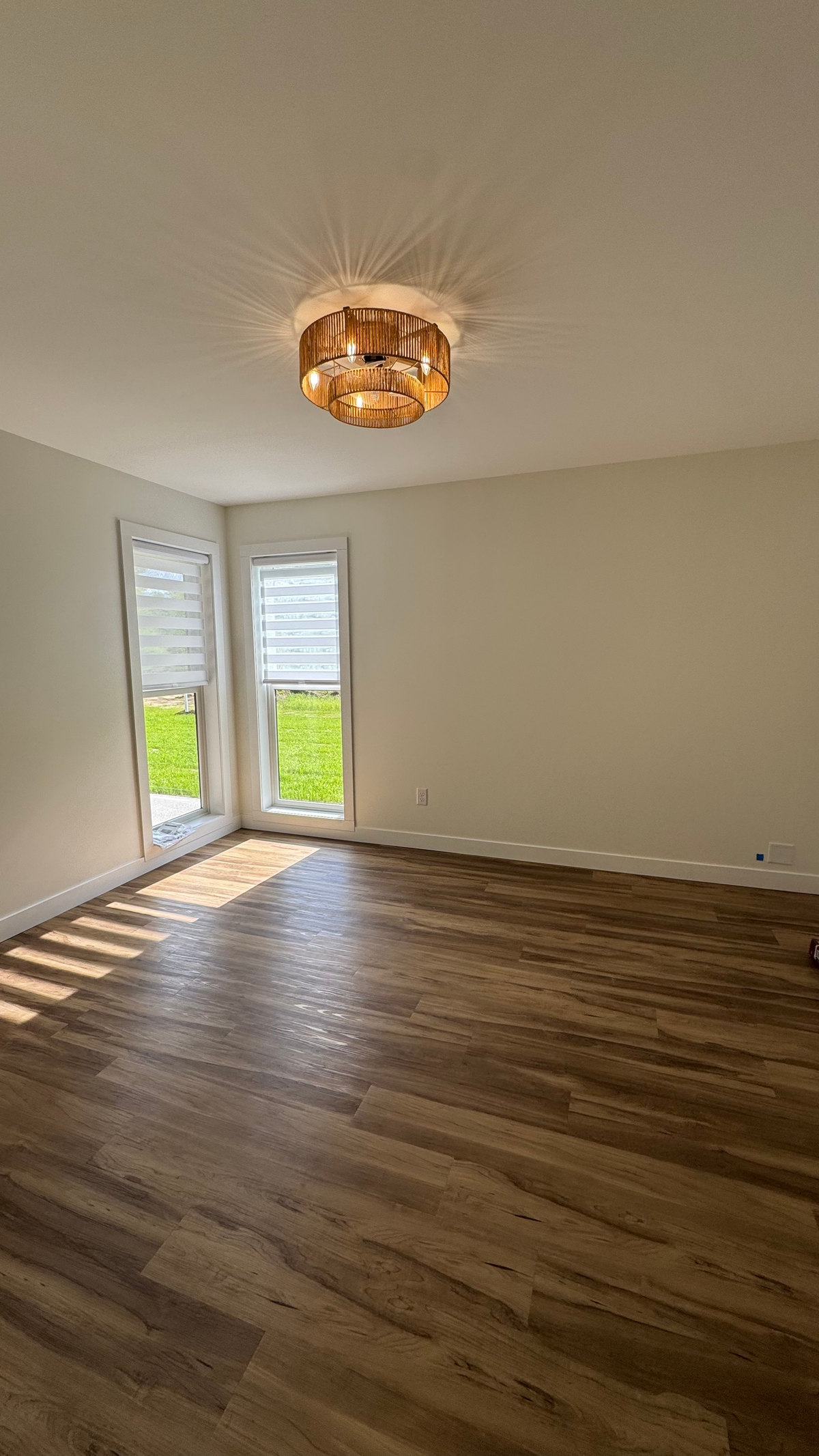 Light-colored walls and ceiling in an unfurnished room with two tall corner windows, a round pendant light and wood-look flooring.